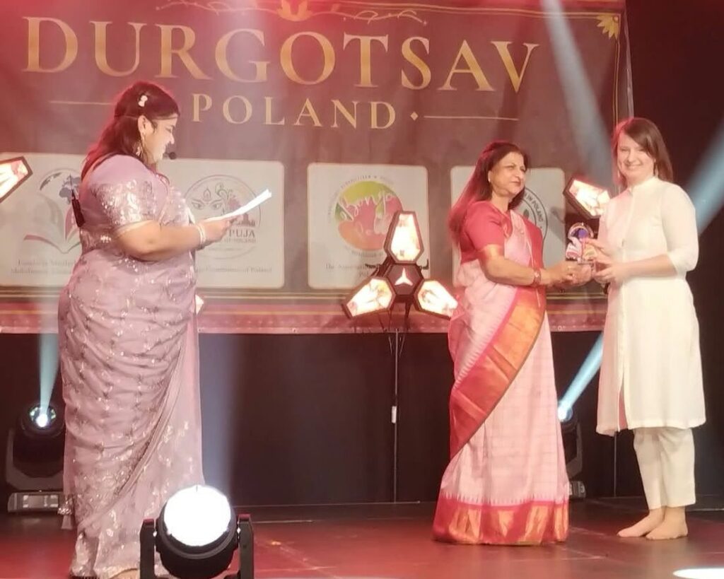 A laureate receives her glass trophy on stage at Durgotsav Poland