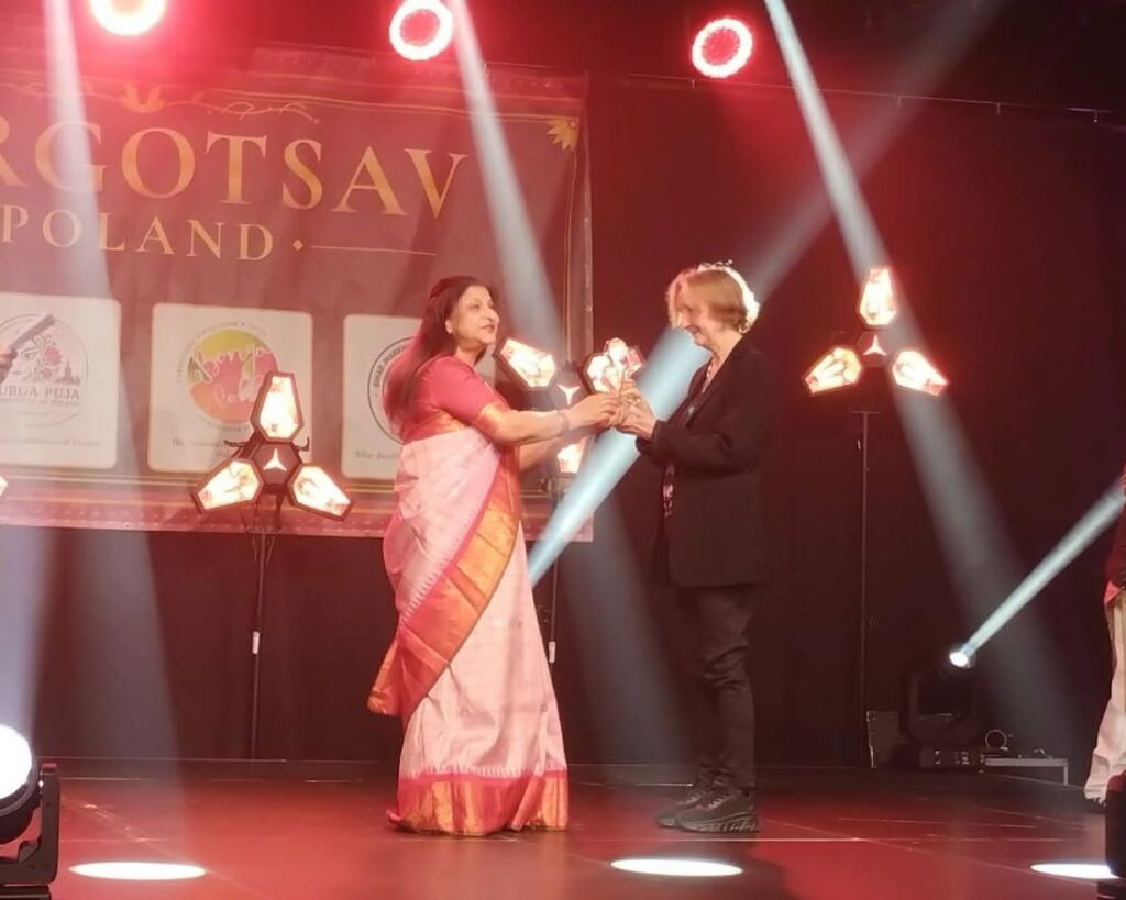 A laureate receives her glass trophy on stage under stage lights